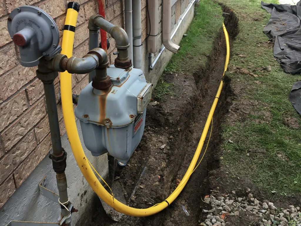 A yellow gas pipe runs from the gas meter through a trench to connect the service line
