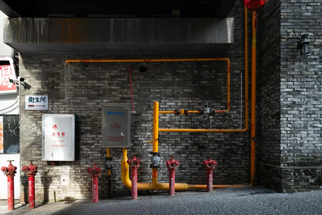 Gas pipes and valves run along a brick wall, with yellow gas lines in a busy commercial area